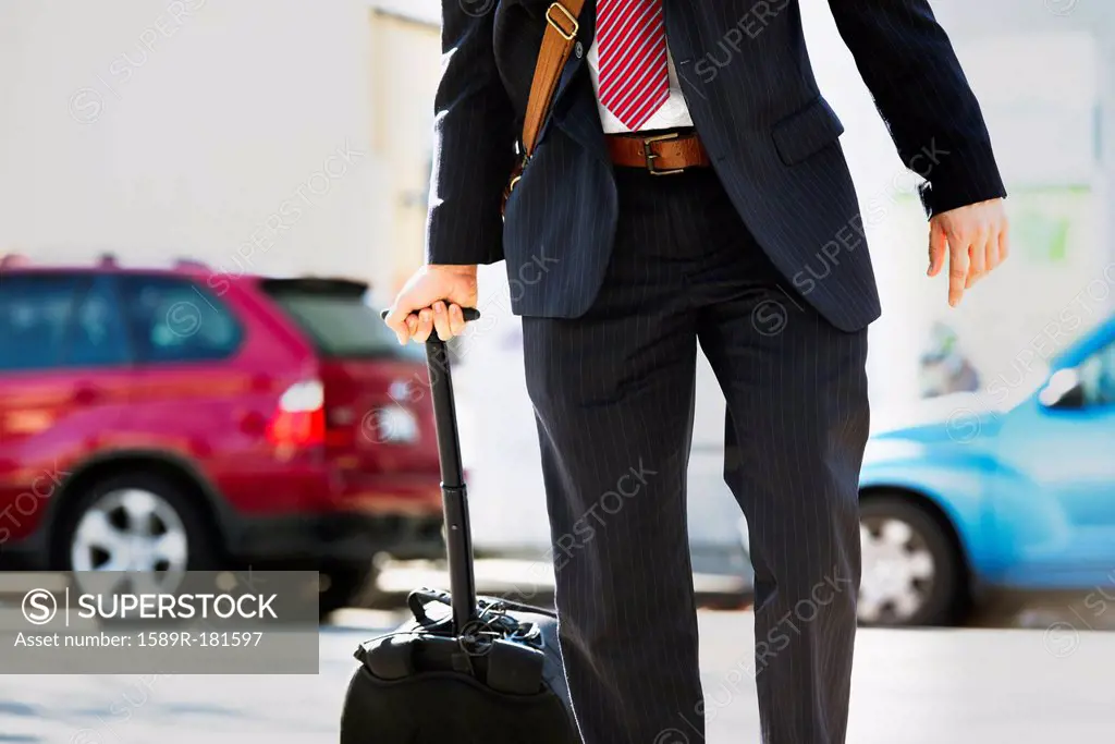 Hispanic businessman rolling luggage
