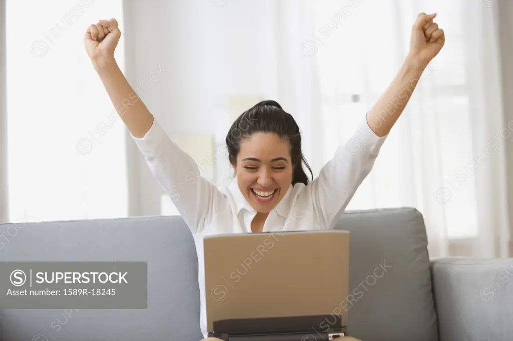 Woman cheering with hands raised holding laptop