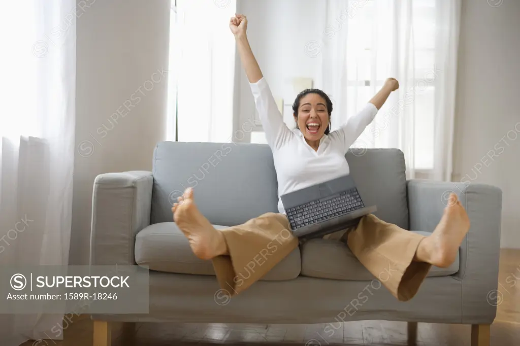 Woman with arms and legs in air holding laptop