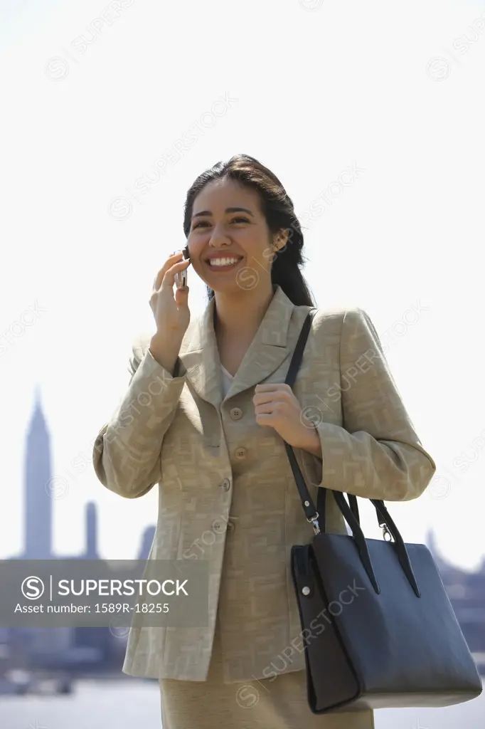 Businesswoman talking on cell phone with city behind her