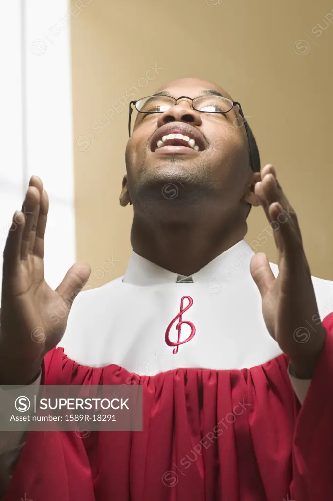 Man in choir robe singing with head and hands raised