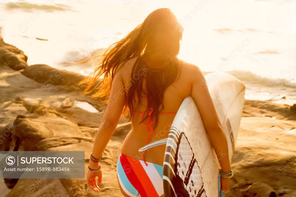 Mixed race woman carrying surfboard on beach