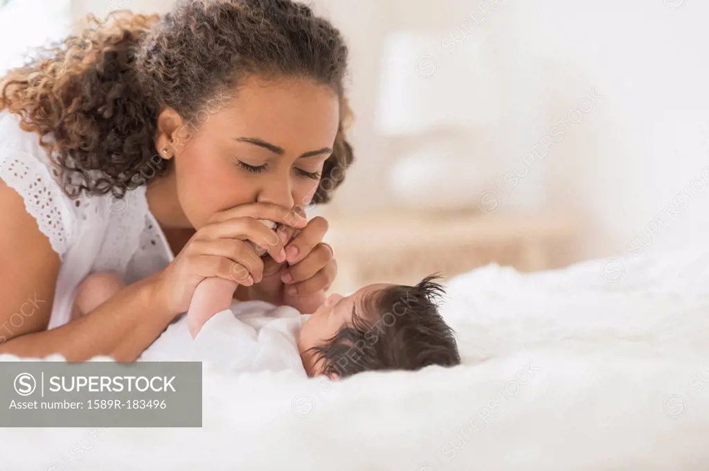 Hispanic mother playing with infant on bed