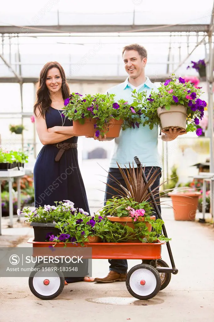 Caucasian couple carrying potted flowers in plant nursery