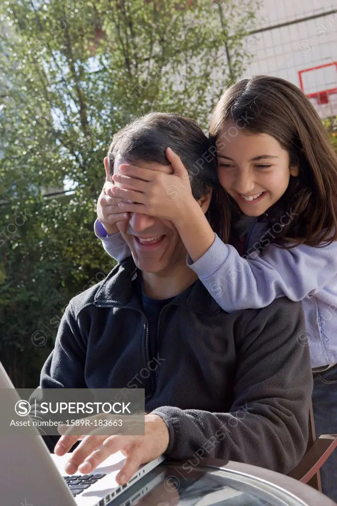 Hispanic girl covering father's eyes