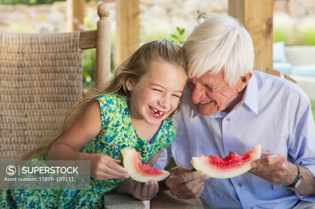 Caucasian man and granddaughter eating watermelon