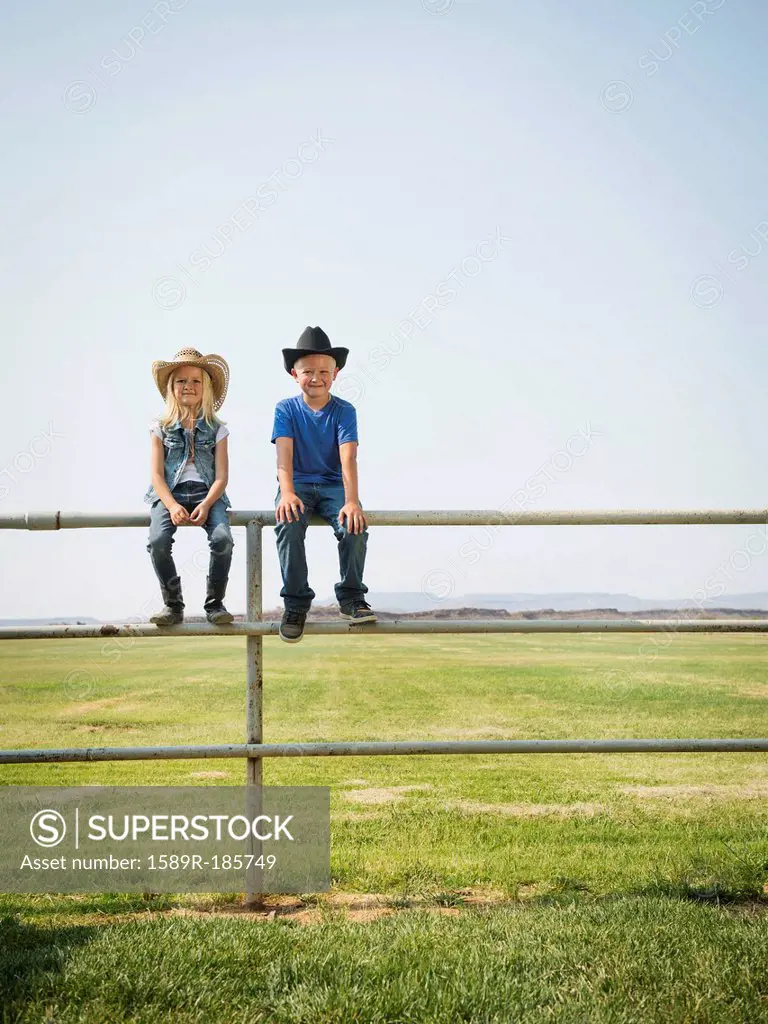 Caucasian children sitting on fence on farm