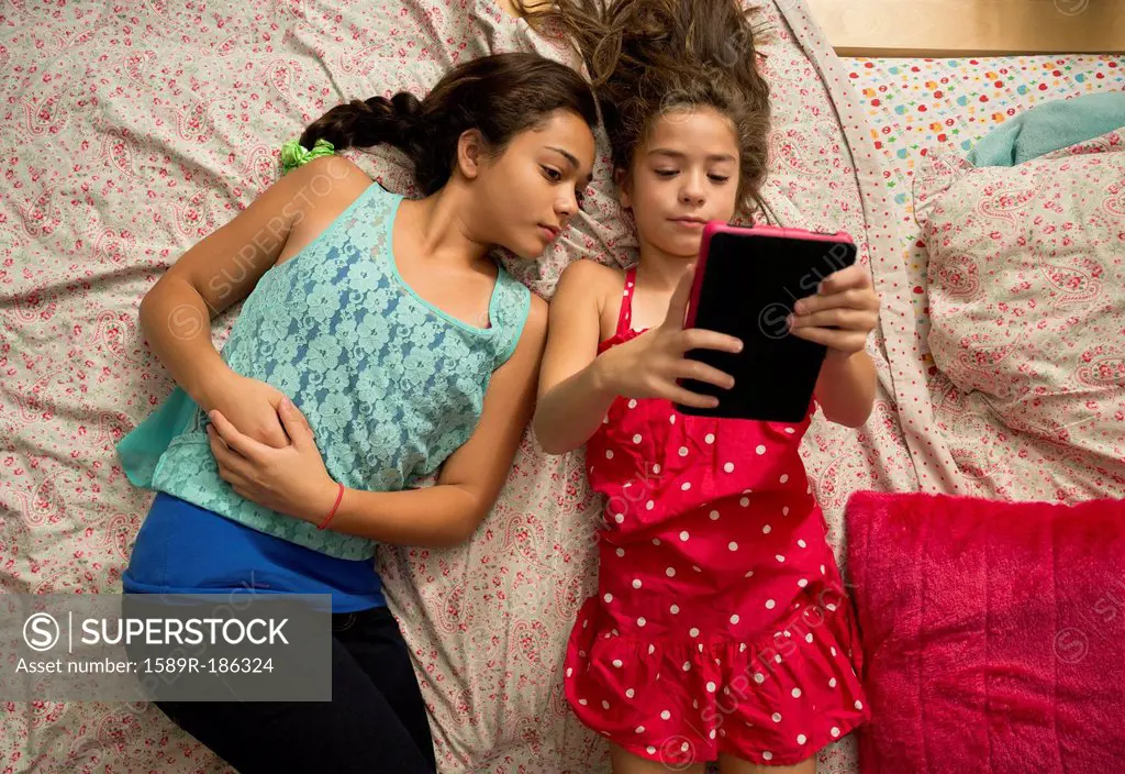 Mixed race sisters using digital tablet on bed