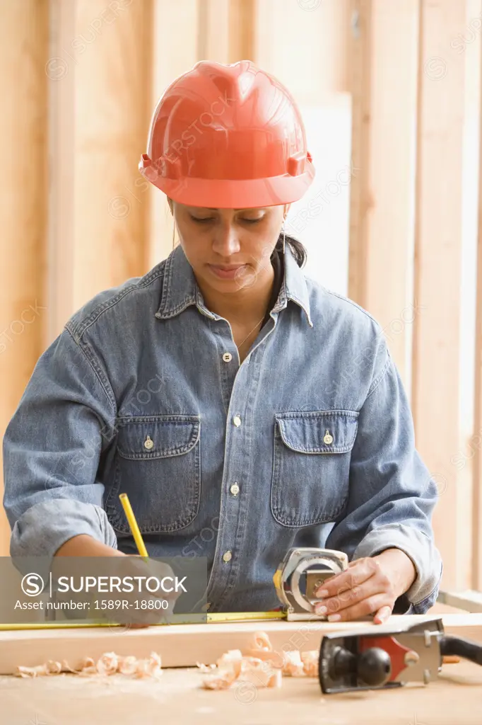 Female construction worker measuring wood with tape measure