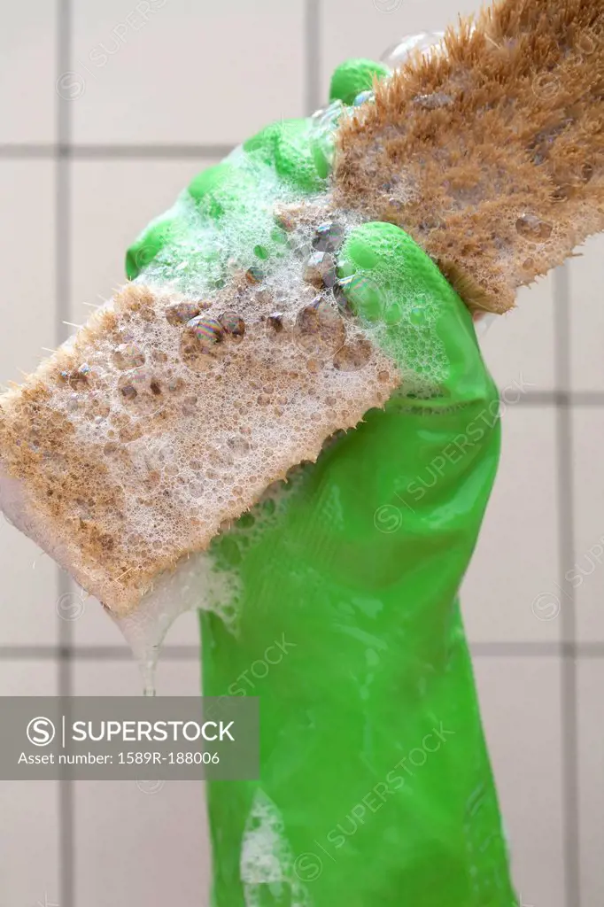 Close up of rubber glove holding sudsy cleaning brush