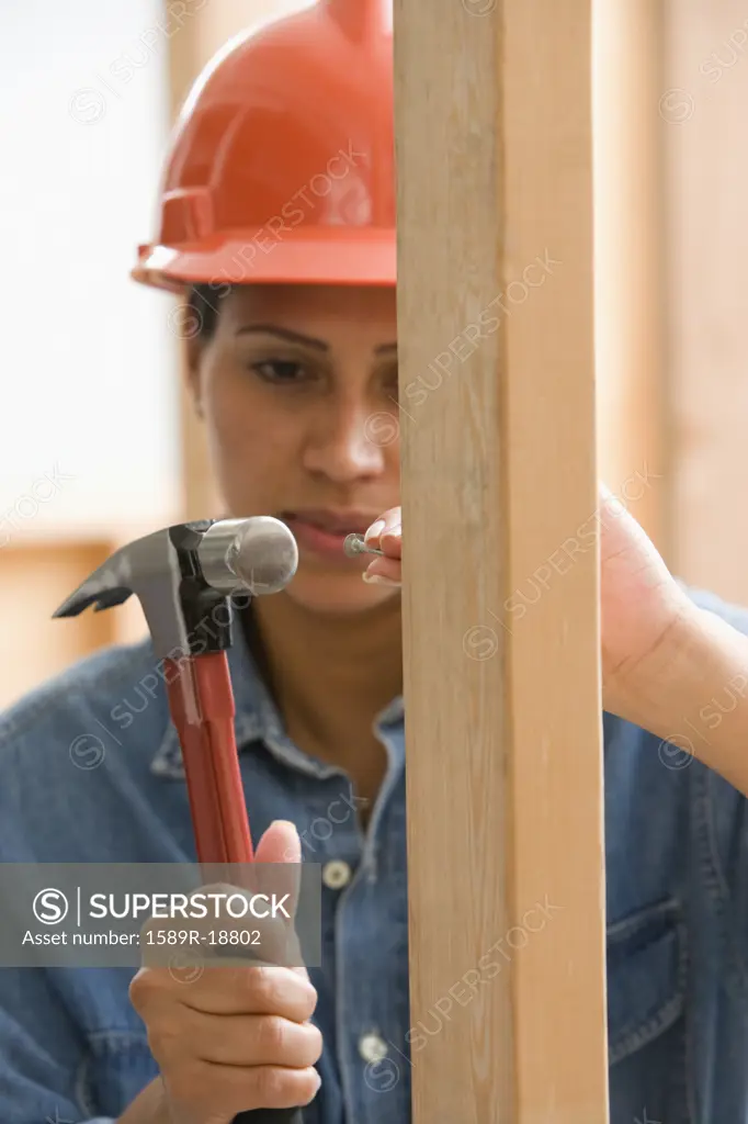 Female construction worker hammering nail into framework