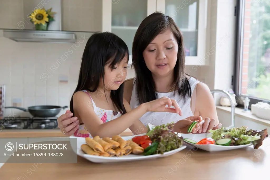Asian mother and daughter eating in kitchen