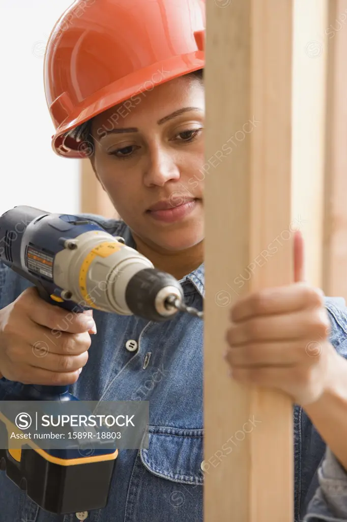 Female construction worker drilling into framing