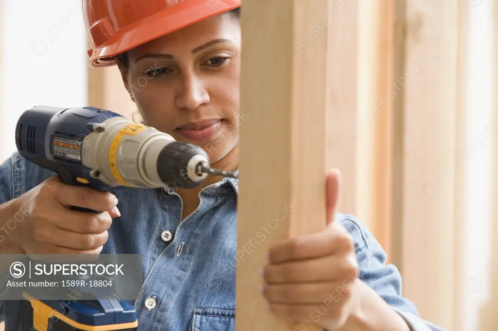 Female construction worker drilling into framing