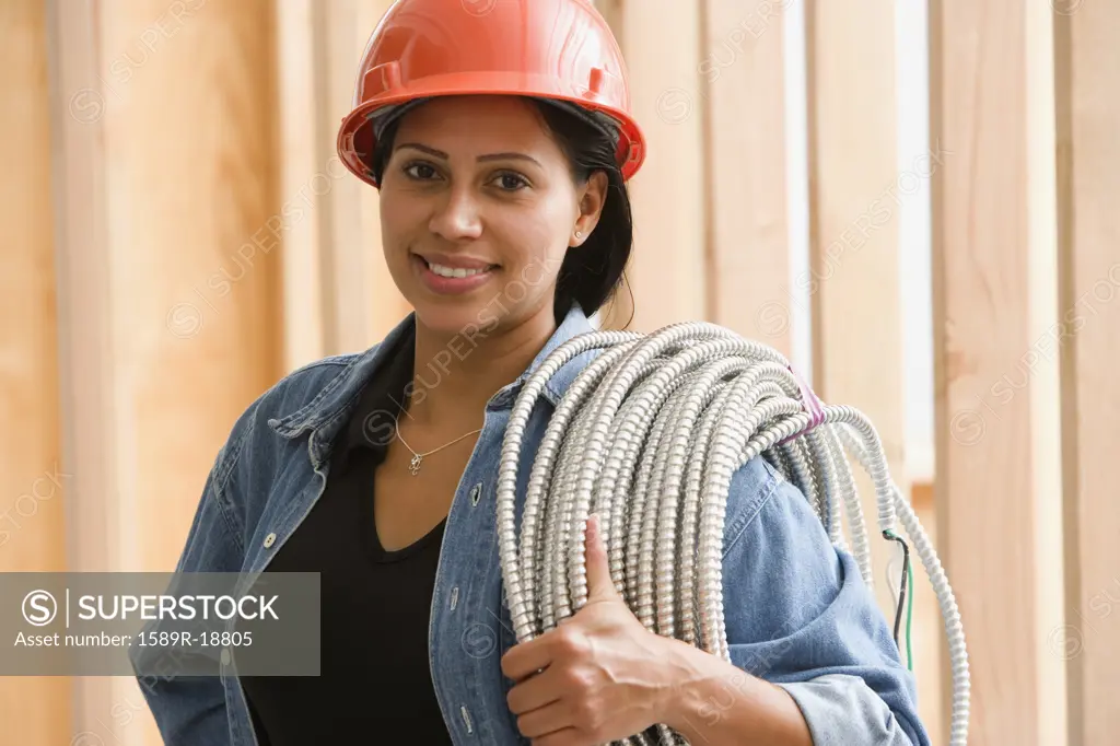 Portrait of female construction worker carrying wiring on shoulder