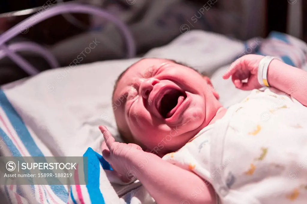 Caucasian newborn baby crying in hospital crib