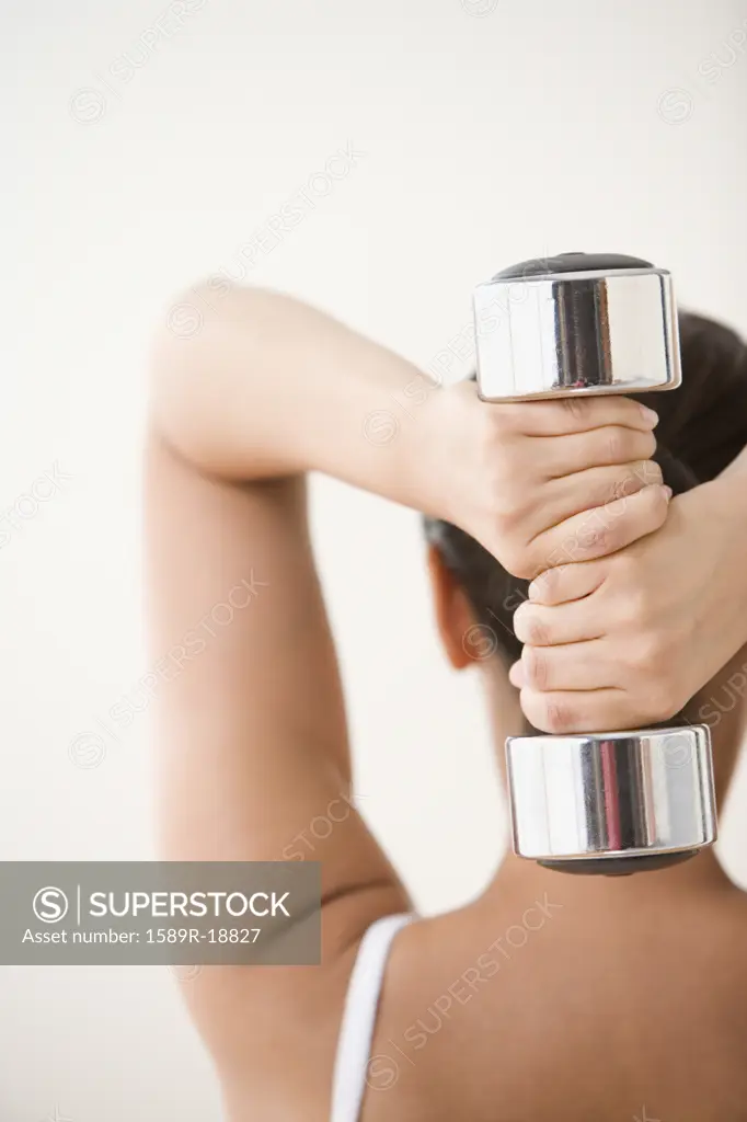Rear view of woman exercising with dumbbell behind head