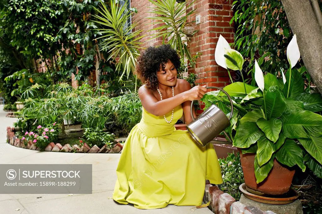 Mixed race woman watering plants in courtyard