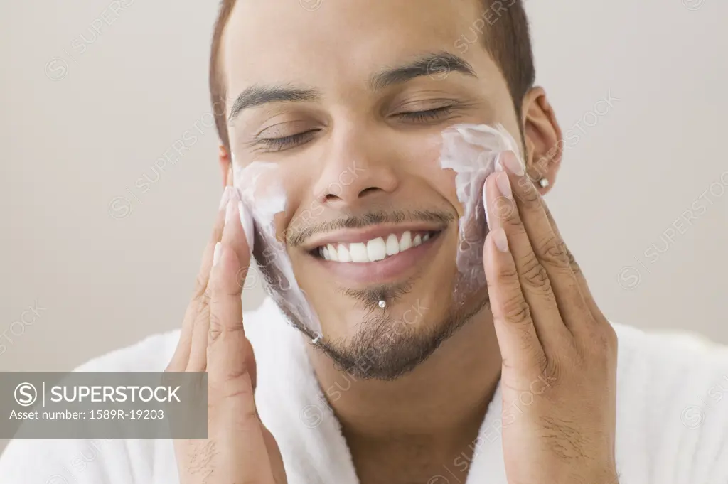 Young man spreading shaving cream on his cheeks