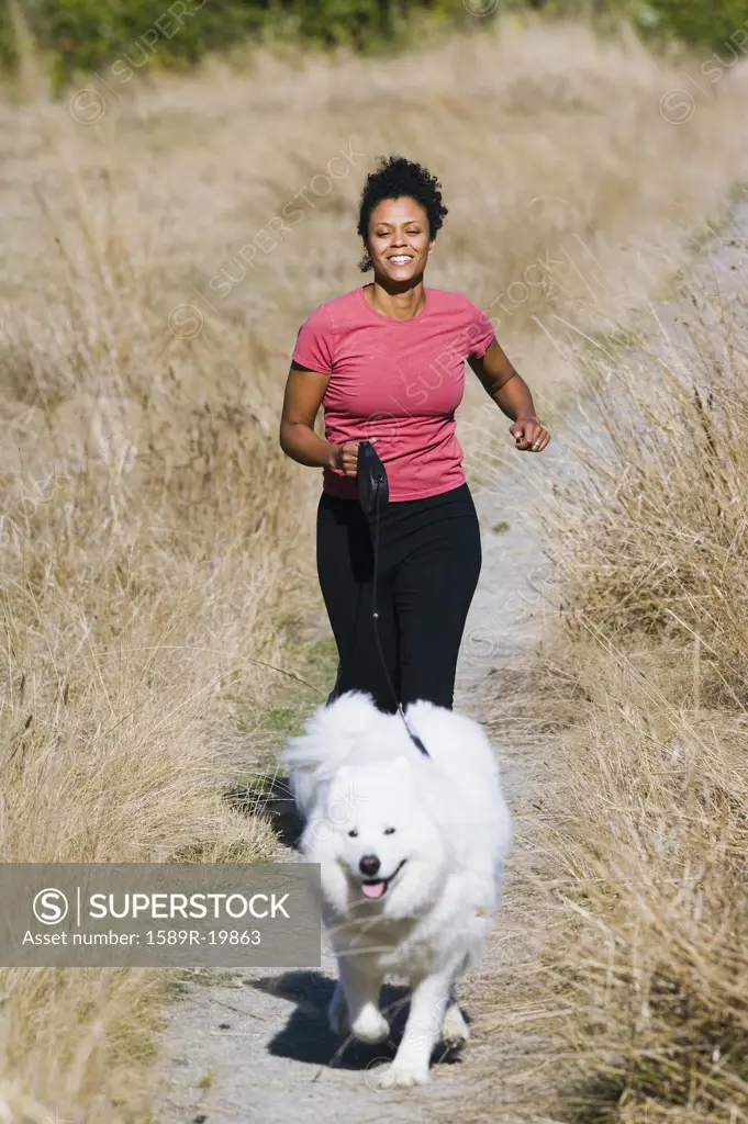 Young woman jogging with her dog on gravel path