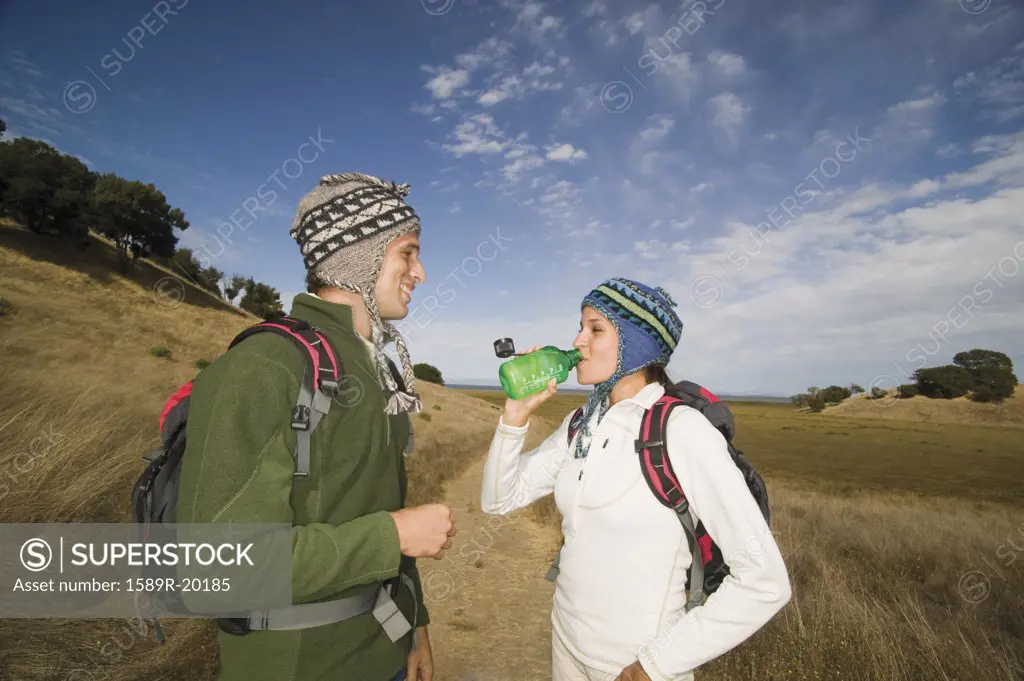 Couple wearing caps and backpacks drinking