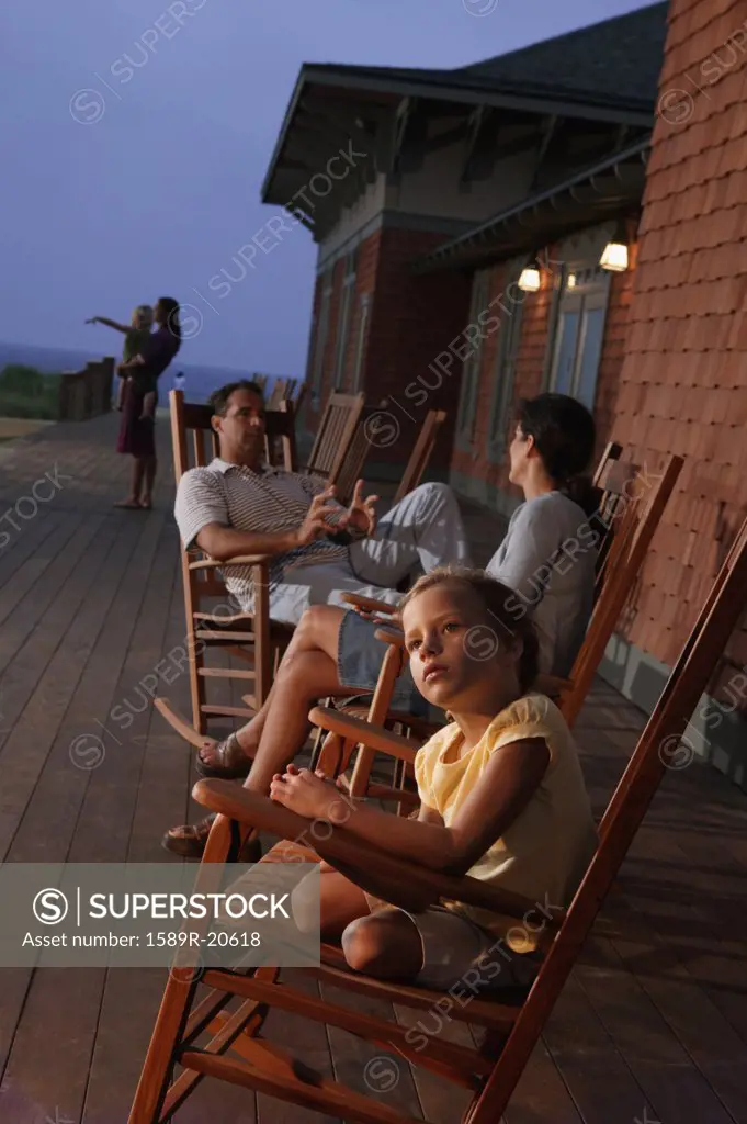 Family sitting in wooden rocking chairs at dusk