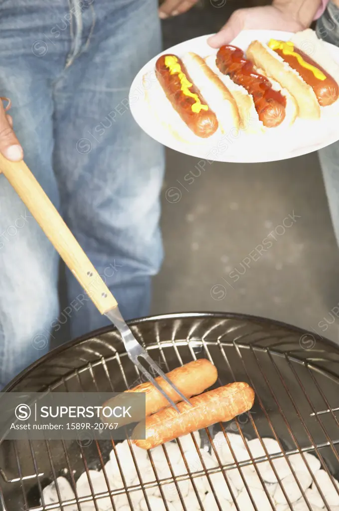 Person cooking sausages on a barbeque grill