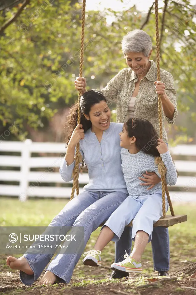 Hispanic mother and daughter sitting on a swing with grandmother pushing, Richmond, Virginia, United States