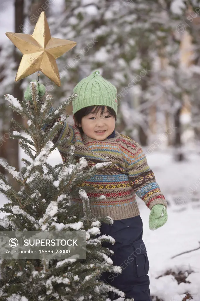 Young Asian girl with Christmas tree in snow outdoors