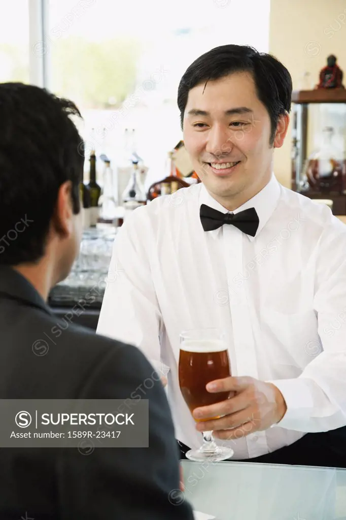 Asian male bartender serving man drink at bar
