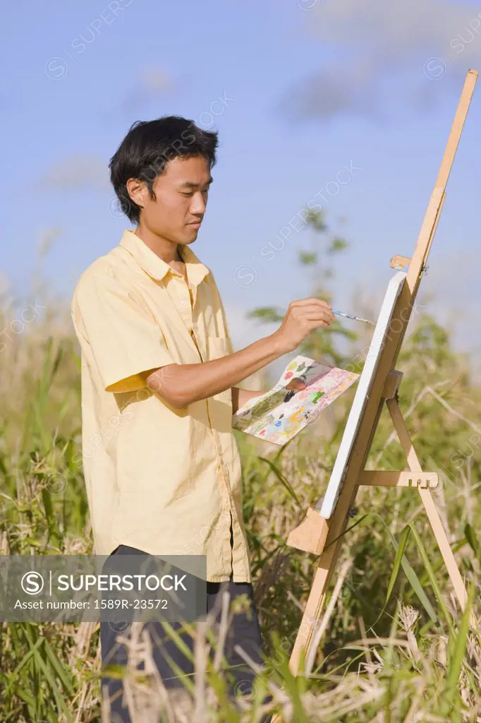 Asian man painting at easel outdoors, Florianopolis, Brazil
