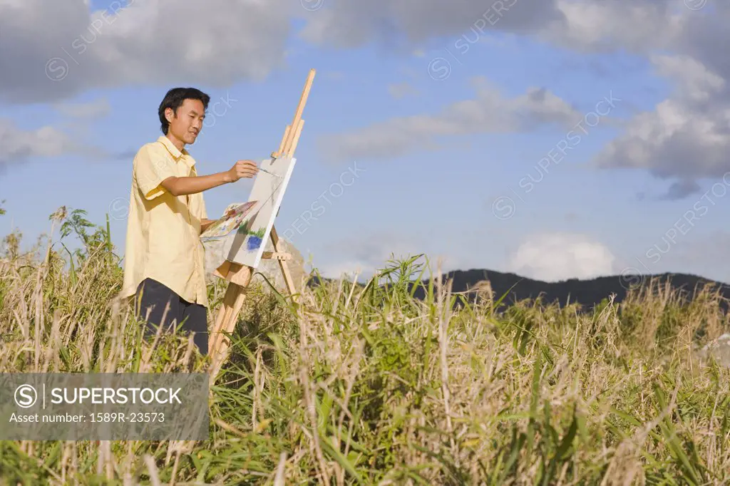 Asian man painting at easel outdoors, Florianopolis, Brazil