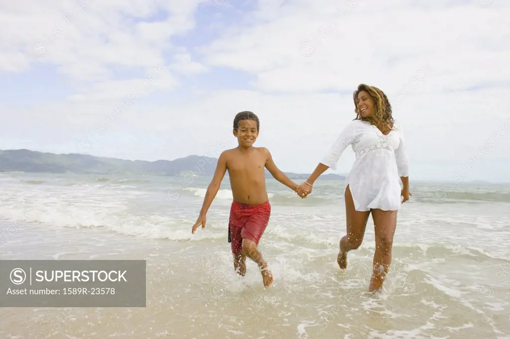 African mother and son running in the surf, Florianopolis, Brazil