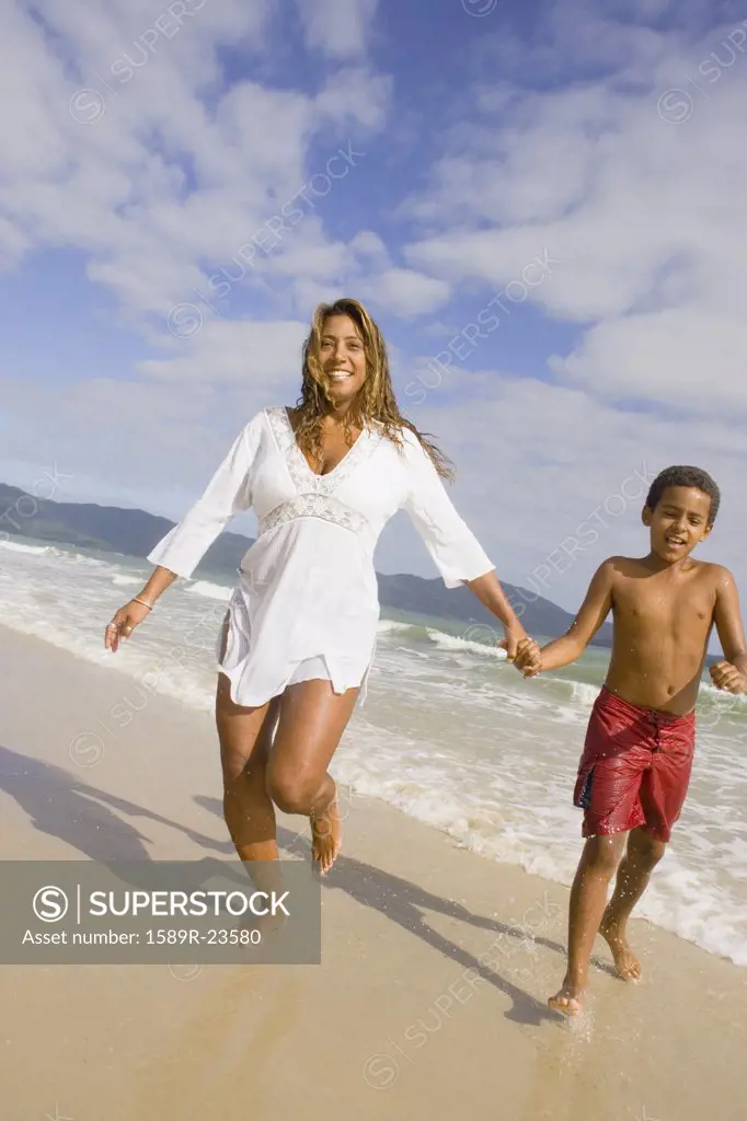 Hispanic mother and son running in the surf, Florianopolis, Brazil