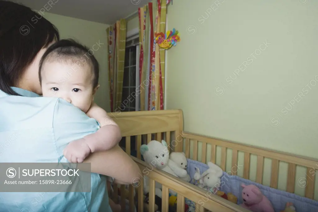 Mother holding Asian baby next to crib