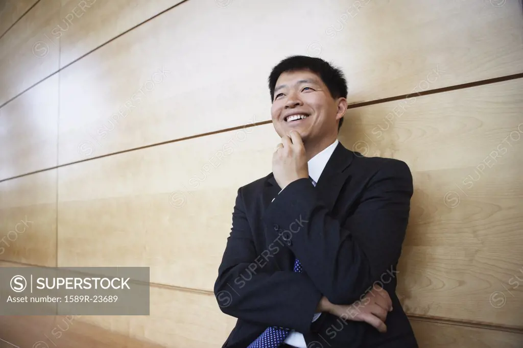 Asian businessman leaning on the wall smiling