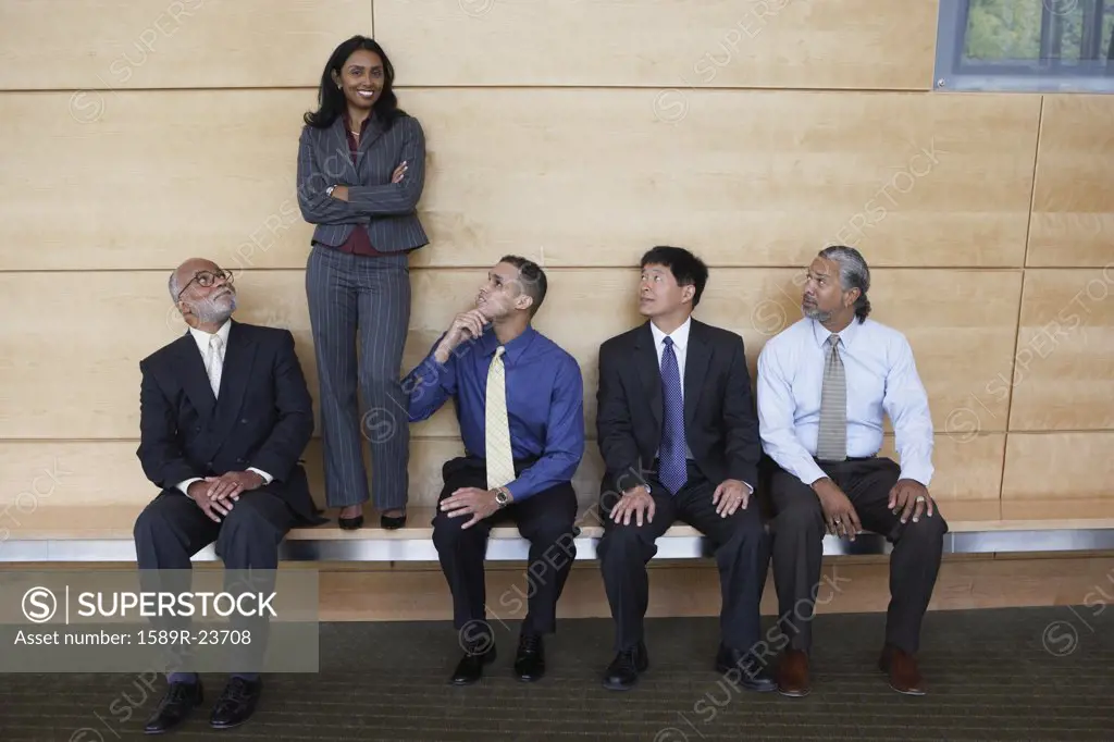 Businesswoman standing on a bench with co-workers looking at her