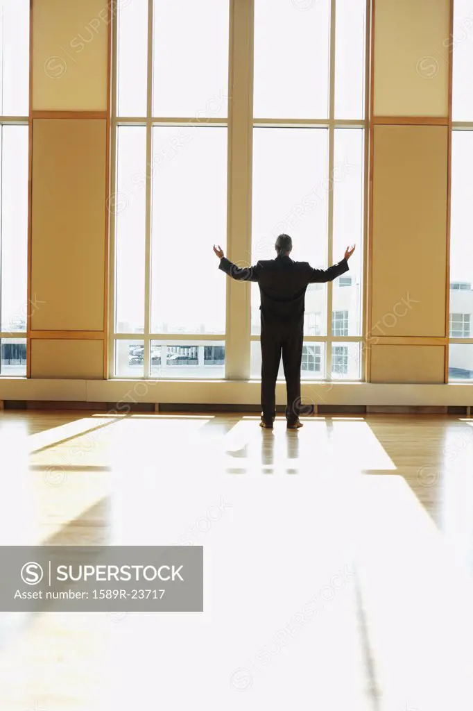 Businessman standing in sunlit room with arms outstretched, North Bethesda, Maryland, United States