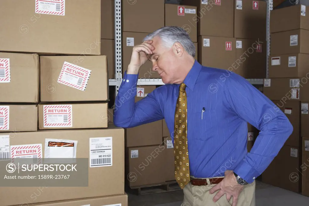 Businessman in warehouse with his head in his hand