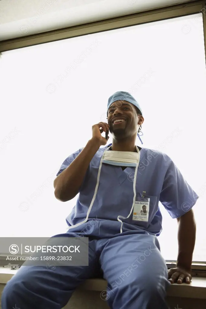 African male surgeon sitting in window alcove with cell phone