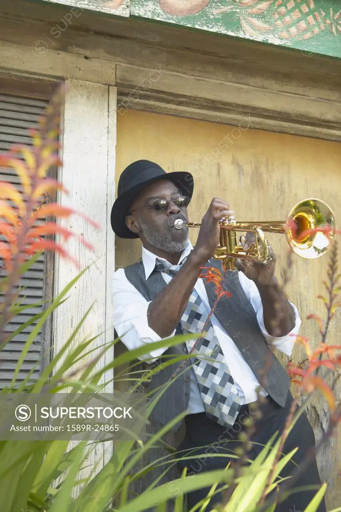 Senior African man playing the trumpet while leaning in a doorway, Oakland, California, United States