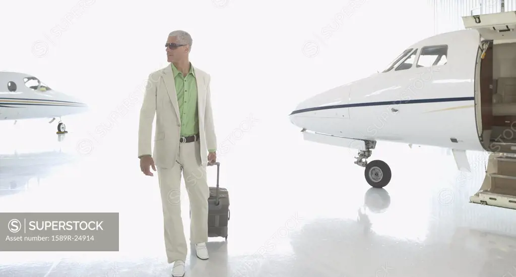Man walking with suitcase in airplane hanger, Nobato, California, United States