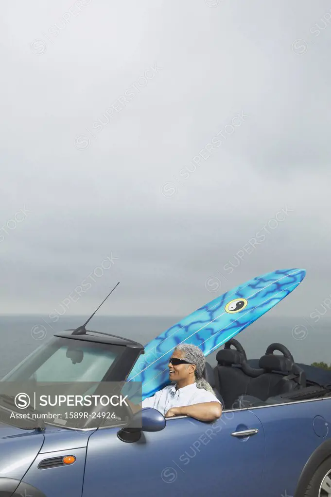 Senior man driving a convertible with a surfboard in it, Oakland, California, United States