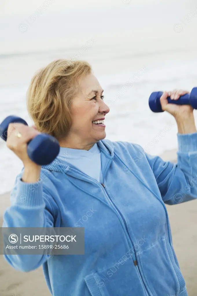 Senior woman lifting weights at the beach