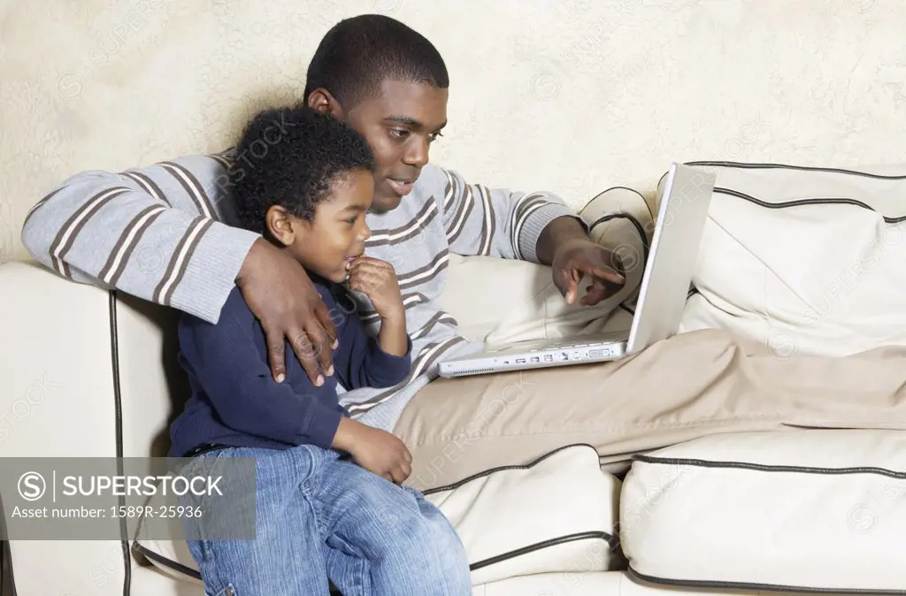African American father and young son with laptop on sofa
