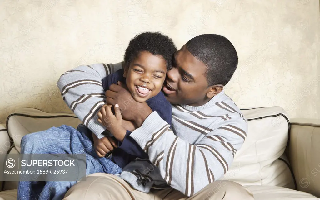 African American father and young son playing on sofa