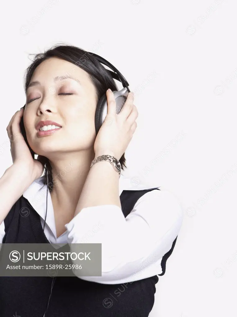 Studio shot of Asian woman listening to music with headphones