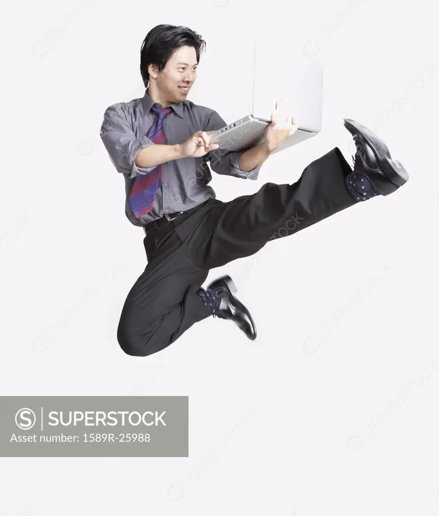 Studio shot of Asian businessman jumping in air with laptop