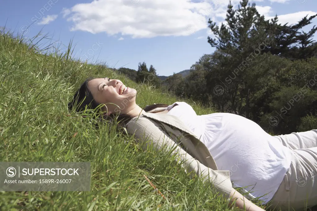 Pregnant Asian woman laying in the grass