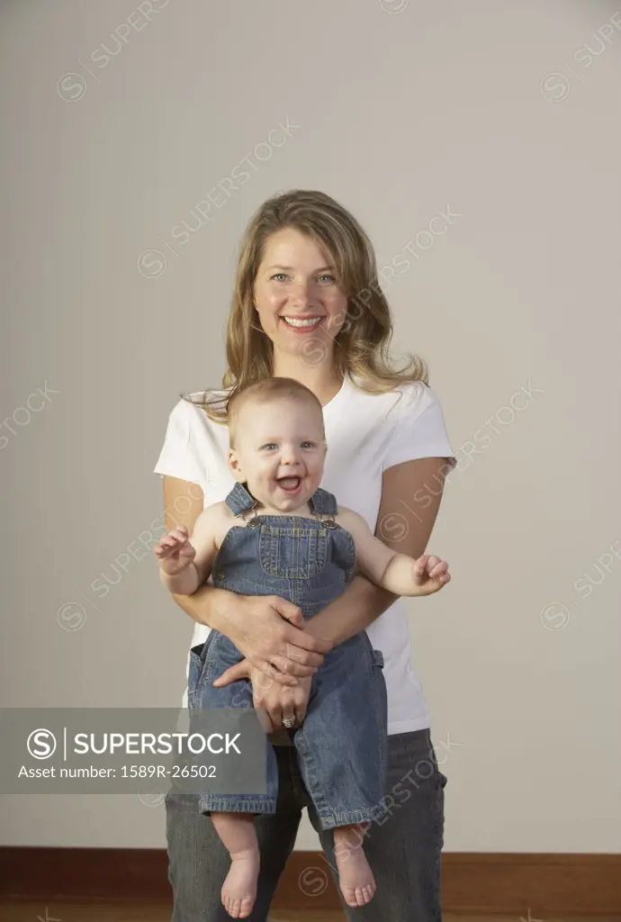 Mother holding laughing baby in overalls